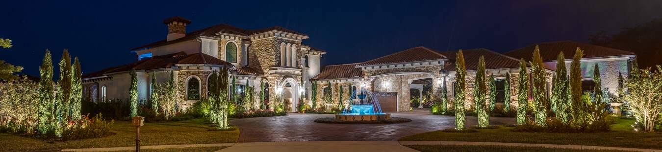 A luxurious house and garden illuminated beautifully at night with elegant outdoor lighting.